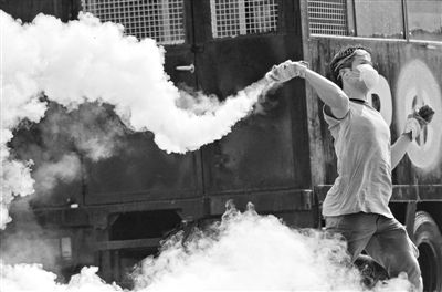 12月2日，泰國曼谷，一名反政府示威者在總理府附近向負責執(zhí)勤的警察投擲催淚彈。英拉請求示威者不要再試圖占領政府工作部門，不要逼迫政府工作人員選邊站。