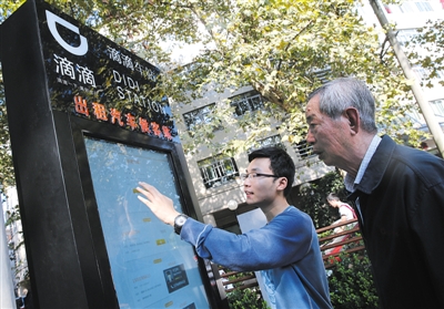 10月15日，滴滴工作人員（左）指導(dǎo)乘客使用“滴滴車站”的電子屏預(yù)約出租車。