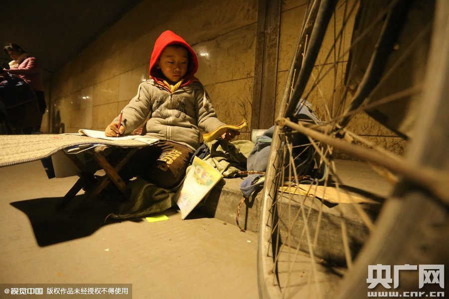 2015年11月8日晚，鄭州，7歲男孩涵洞橋下陪父母練攤，路邊燈下坐小馬扎上寫作業(yè)。