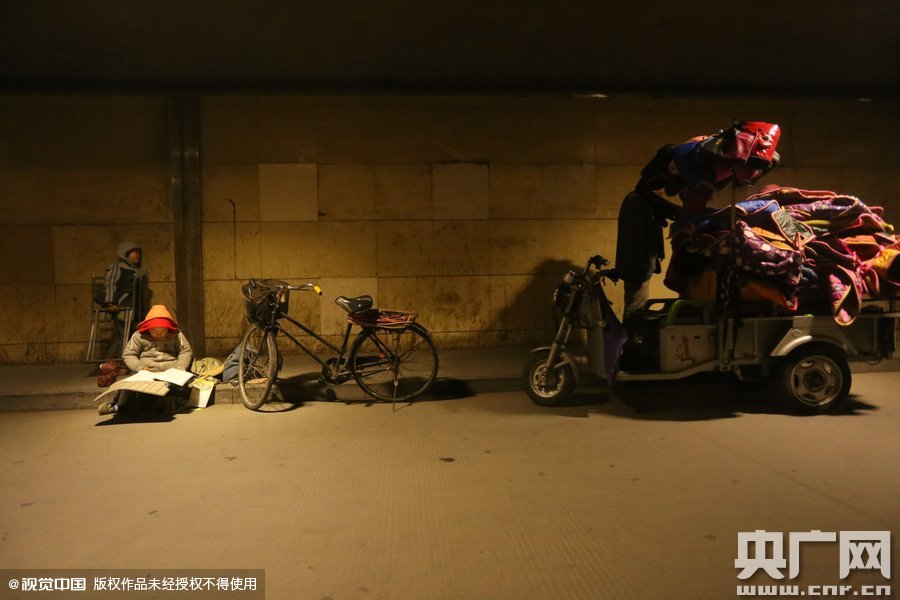 2015年11月8日晚，鄭州，7歲男孩涵洞橋下陪父母練攤，路邊燈下坐小馬扎上寫作業(yè)。