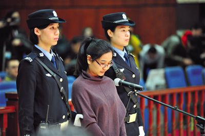 被告人盧梅低著頭，站在朝陽(yáng)法院刑事審判庭的被告席上。