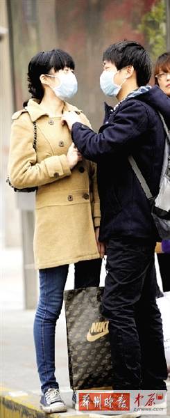 公交站臺(tái)上，一對(duì)年輕人戴著口罩，系緊衣領(lǐng)。